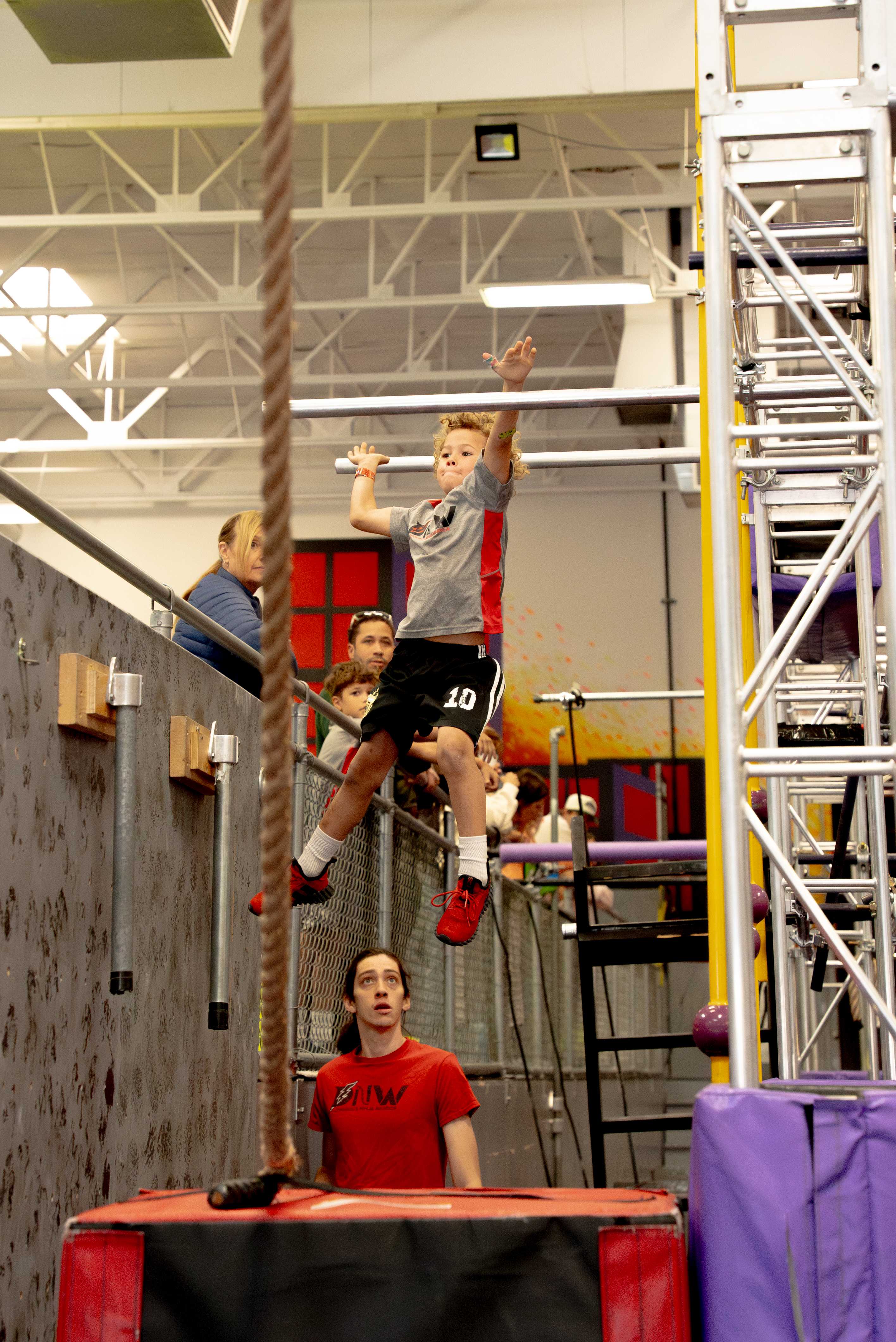 Young NES athlete mid-air reaching for a rope as family watches from the railing